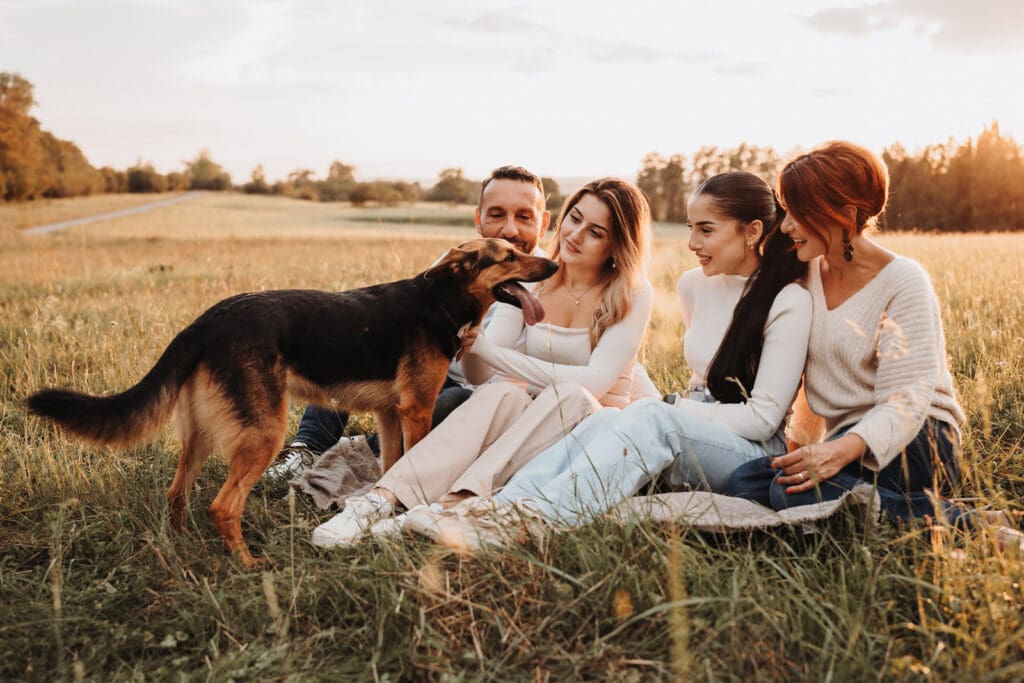 Familie sitzt bei Sonnenuntergang zusammen mit ihrem Hund bei einem Fotoshooting